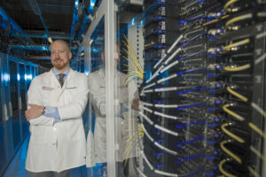 Alexander Pearson, MD, PhD, standing next to a computer server.